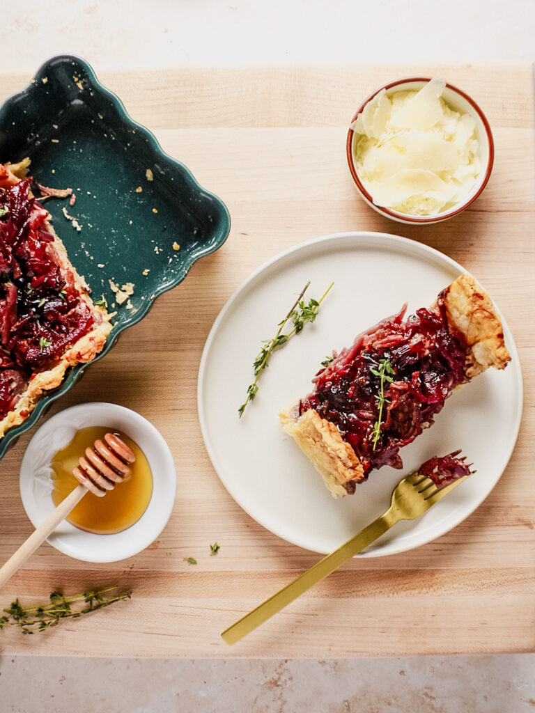 Red onion tart in green tart dish with honey in a plate